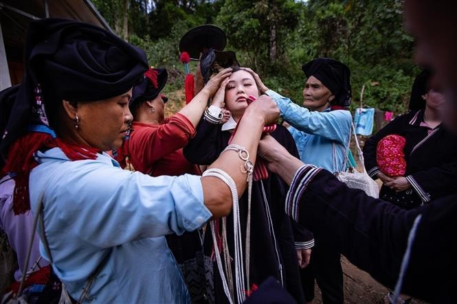 Female relatives dress the bride in multiple layers of traditional attire. (Photo: VNA)