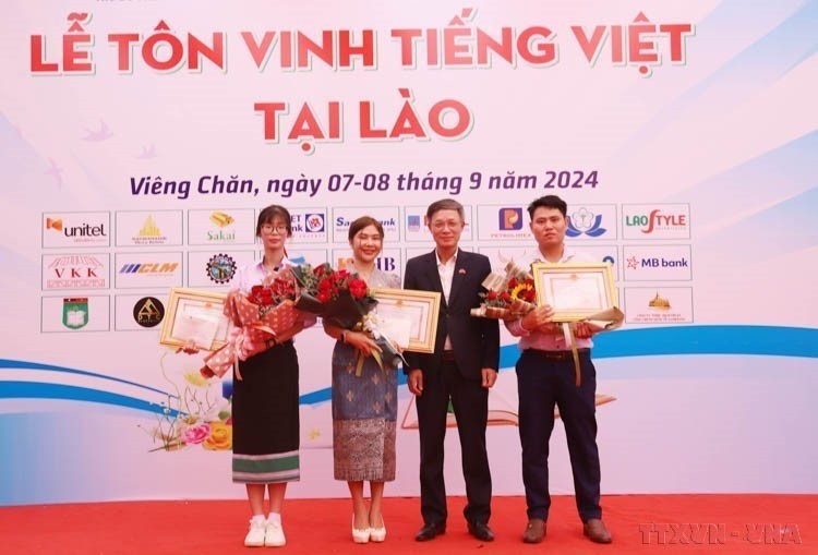 Vietnam’s Chargé d’Affaires in Laos Phan Minh Chien presents certificates of merit and awards to three finalists of the “Vietnamese language ambassadors abroad 2024” contest at a ceremony honoring the Vietnamese language in Laos. (Photo: VNA)