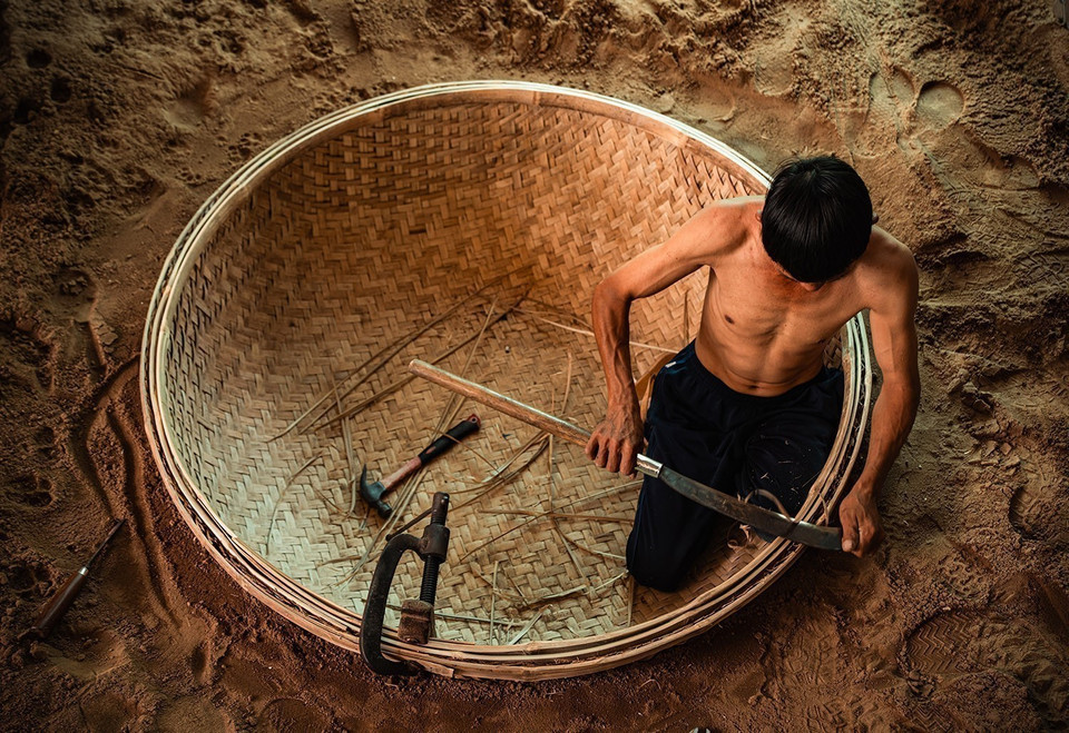 To shape the boat, a round hole is dug into the ground, where the woven bamboo base is placed for further shaping. (Photo: VNA)