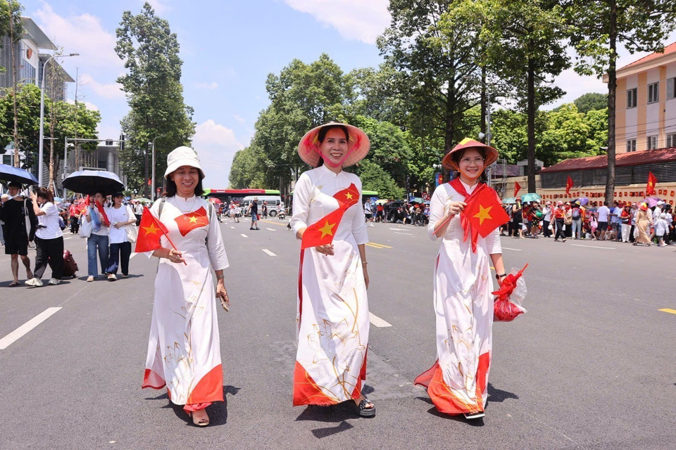 People from different regions of the country wear the traditional ao dai and carry national flags. (Photo: VNA)