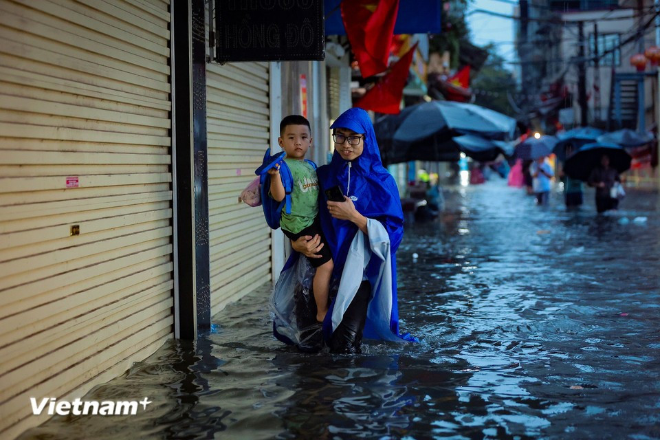 Residents wade through flooded streets to pick up children. (Photo: Hoai Nam/Vietnam+)