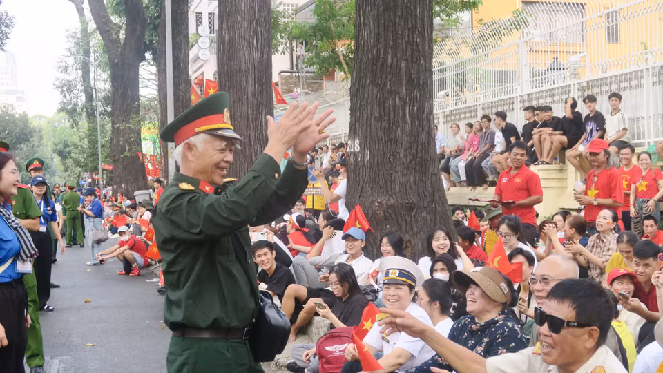 A veteran leads the crowd in singing "As if Uncle Ho Were Here on the Great Victory Day" while waiting for the parade. Photo: VNA