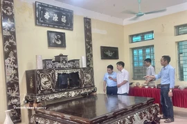 Artisan Vu Van Vinh from Chuyen My commune introduces to visitors a set of mother of pearl inlaid lacquer furniture including a platform bed, tea cabinet, and lacquered horizontal boards and parallel sentences made by his family, worth more than 3 billion VND. (Photo: VNA) 