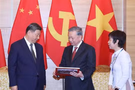 Party General Secretary To Lam (centre) presents Party General Secretary and President of China Xi Jinping with a photo book compiled by the Vietnam News Agency, featuring remarkable images from Xi’s five visits to Vietnam since 2011, including the current trip. (Photo: VNA)