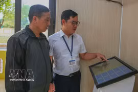 A civil servant at the Van Thang commune Public Administrative Service Centre in Ninh Binh province guides a resident on how to obtain a queue number using the machine. (Photo: VNA) 