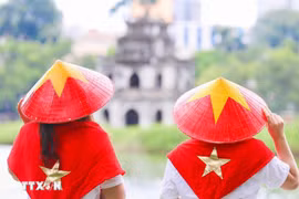 Visitors wearing national flag-themed conical hats at Hoan Kiem Lake, an icon of Hanoi (Photo: VNA)