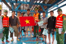 Officers of the Vam Lang border guard station in Dong Thap disseminate information on the prevention of illegal, unreported and unregulated (IUU) fishing and present a national flag to members of a local ship. (Photo: VNA)