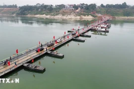 People and vehicles travel across the Lo river pontoon bridge on the morning of February 16. (Photo: VNA) 