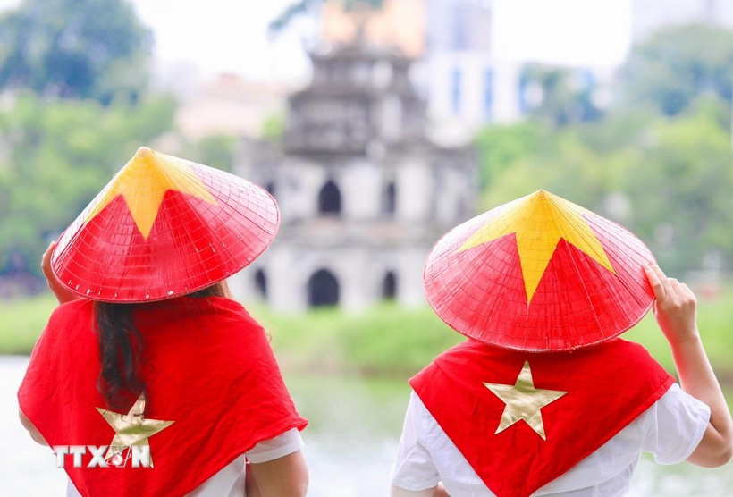Visitors wearing national flag-themed conical hats at Hoan Kiem Lake, an icon of Hanoi (Photo: VNA)