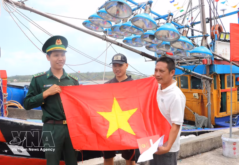 Fishermen receive national flag from a border officer (Photo: VNA)