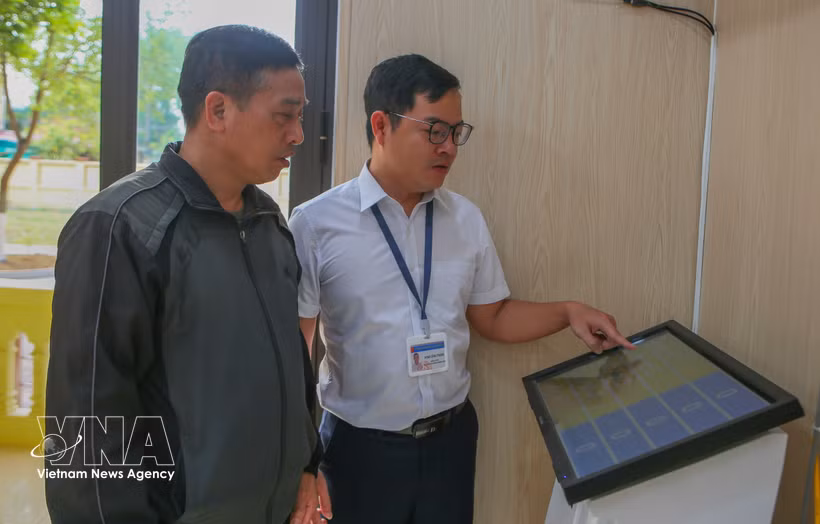 A civil servant at the Van Thang commune Public Administrative Service Centre in Ninh Binh province guides a resident on how to obtain a queue number using the machine. (Photo: VNA) 