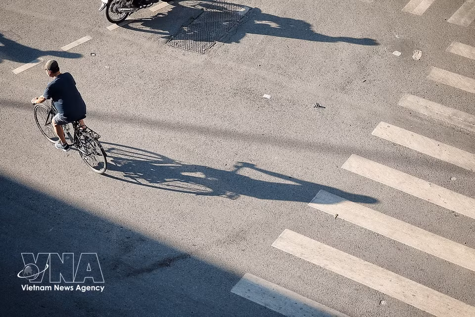 People cycle across the intersection as the first rays of sunlight begin to illuminate the road. (Photo: VNA)