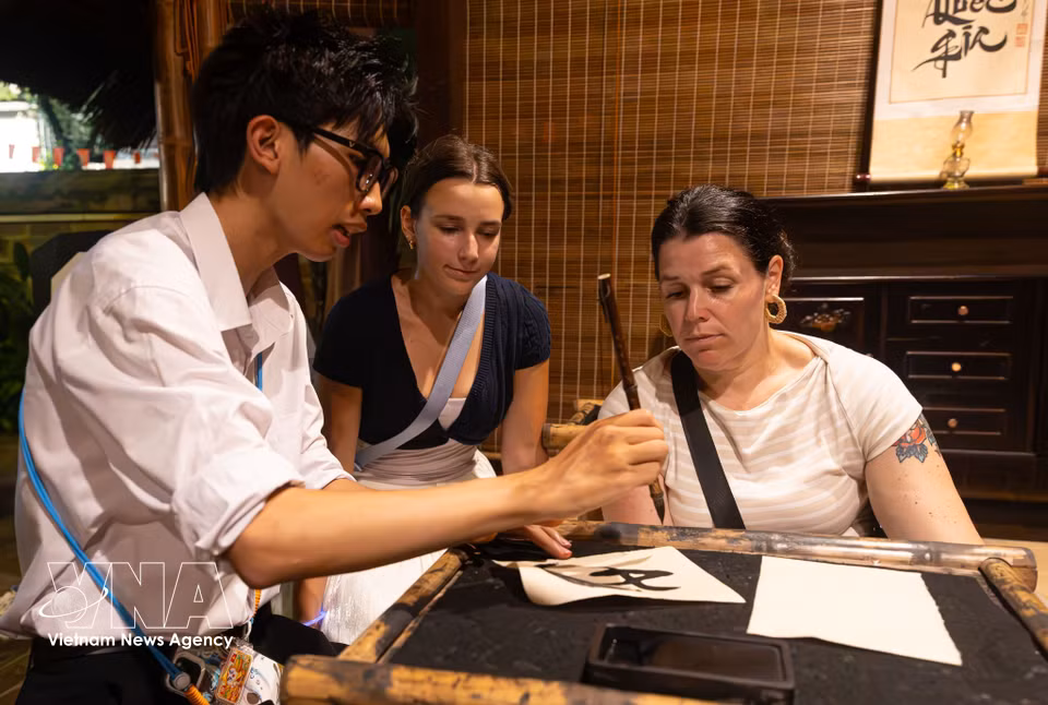 International tourists enthusiastically try brush calligraphy under the guidance of an instructor. (Photo: VNA)