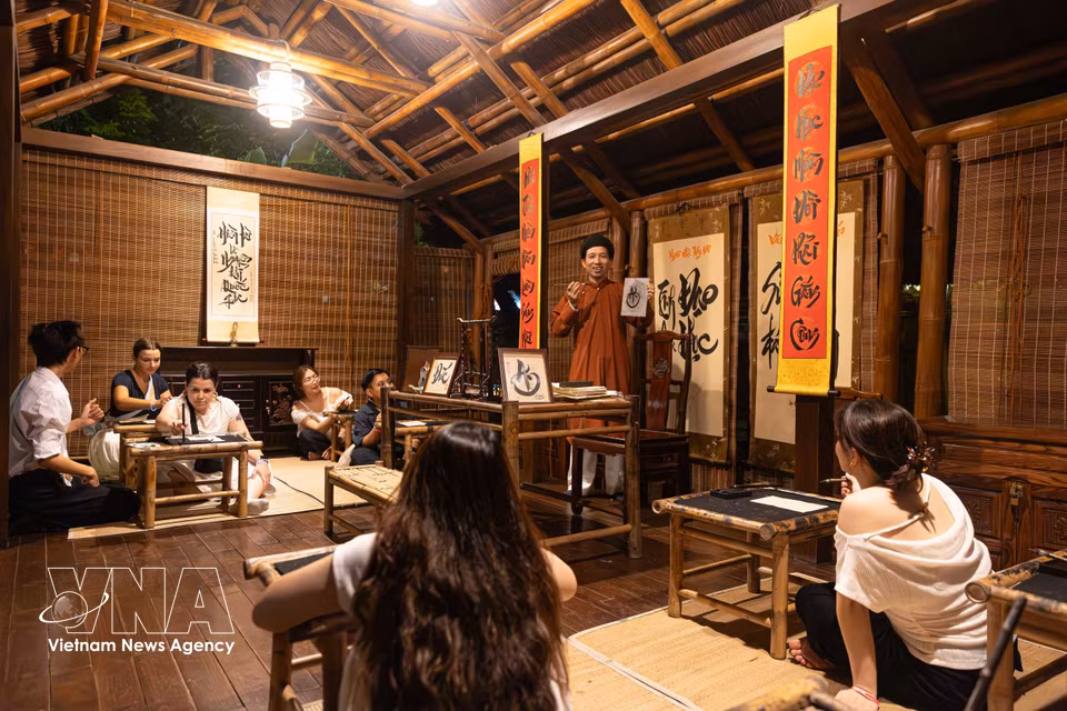 Visitors join a calligraphy class with a calligraphy scholar as part of the “Essence of Education” night tour at the Temple of Literature. (Photo: Published by VNA)