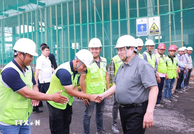 Prime Minister Pham Minh Chinh (R) encourages workers and engineers at the Vietnam Exhibition Fair Centre project site. (Photo: VNA)