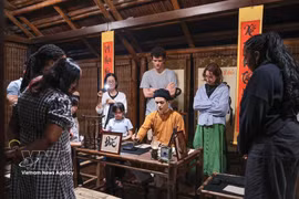 Tourists watch a calligraphy master demonstrate the art in a heritage setting during the Temple of Literature's night tour. (Photo: VNA)