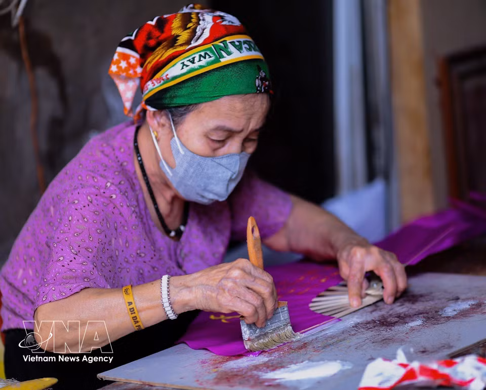 The artisan’s hands gently smooth glue over each layer of paper, preserving the spirit of craftsmanship in every fan. (Photo: VNA)