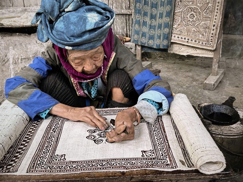 An elderly artisan draws traditional beeswax patterns on hemp fabric. (Photo: VNA)
