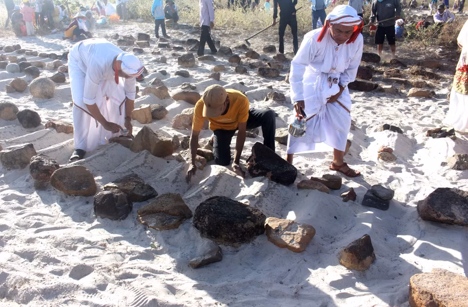 Families conduct the sand-clearing and water-pouring rituals to cleanse the graves. (Photo: VNA)
