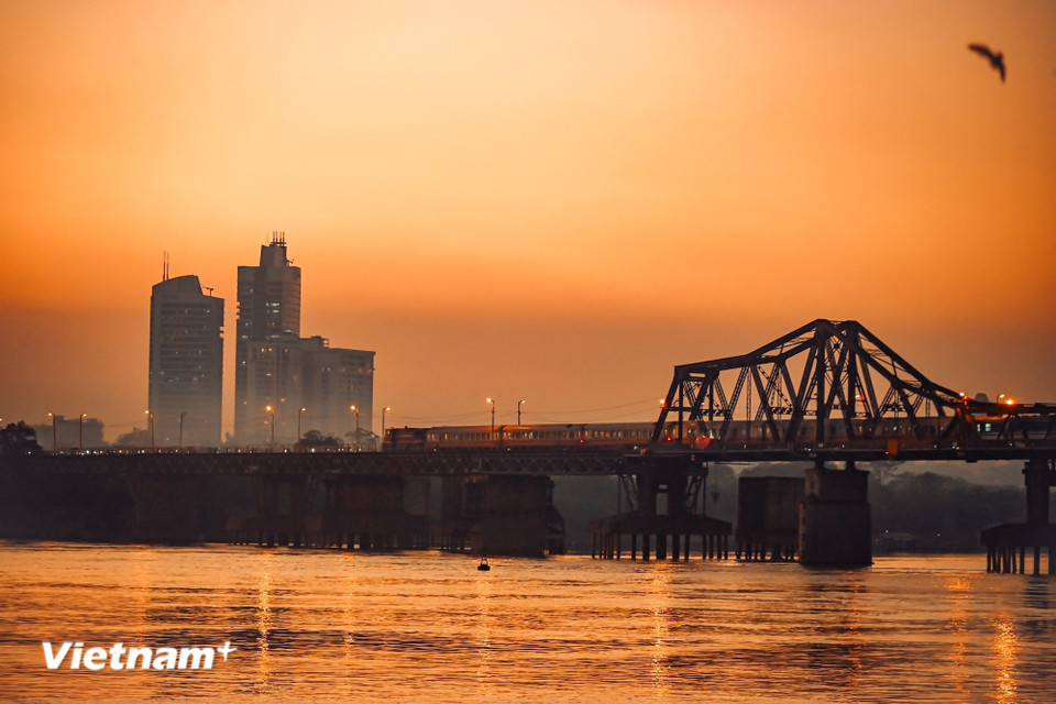 From a distance, Long Bien Bridge comes into view, the sunset dyeing the water crimson as a train slowly makes its way towards the heart of the city. (Photo: Vietnam+)