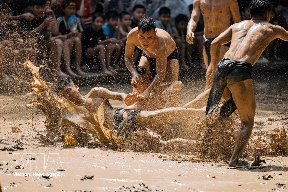 A player falls onto the muddy field following a heavy collision, while teammates and opponents continue chasing the wooden ball. (Photo: VNA)