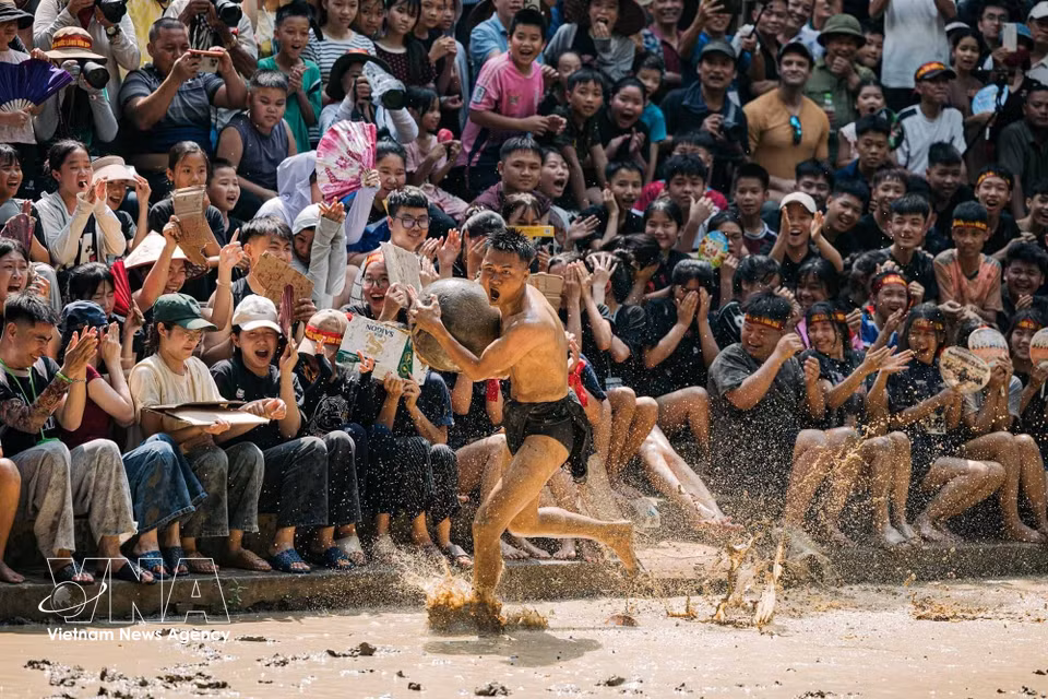 A player sprints across the muddy field while clutching the wooden ball as hundreds of spectators cheer him on. (Photo: VNA)