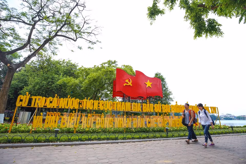 Pedestrians walk pass a banner calling for voters' participation in the elections (Photo: VNA)