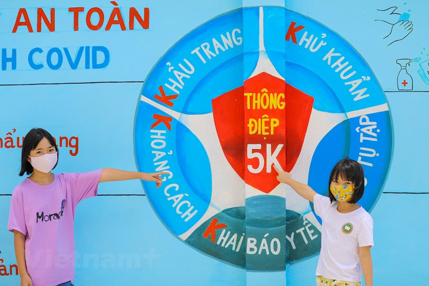 Children poses for photos by a mural painting of 5K (in Vietnamese, which is literally translated as facemask, disinfection, distance, health declaration and no gatherings) message by the Health of Ministry. (Photo: Vietnam+)