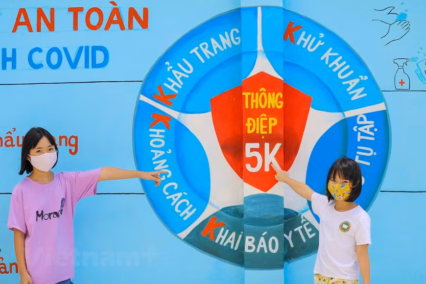 Children poses for photos by a mural painting of 5K (in Vietnamese, which is literally translated as facemask, disinfection, distance, health declaration and no gatherings) message by the Health of Ministry. (Photo: Vietnam+)