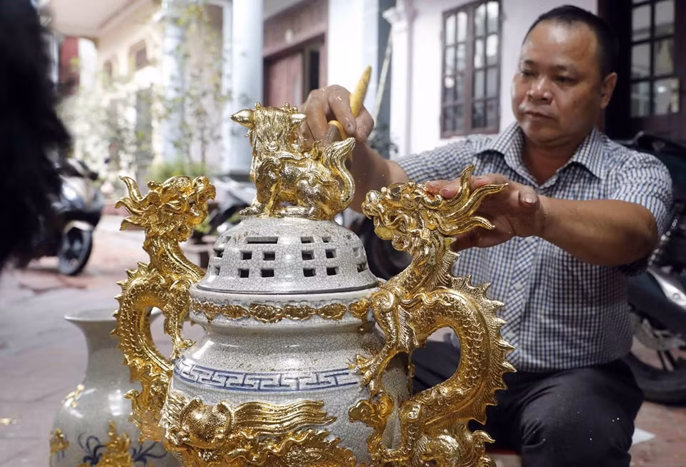 To create a smooth and shiny golden coat for products, gilding craftsmen need to overlay the products with super-thin gold leaves while the paintwork is still wet (Photo: Tran Viet/VNA)