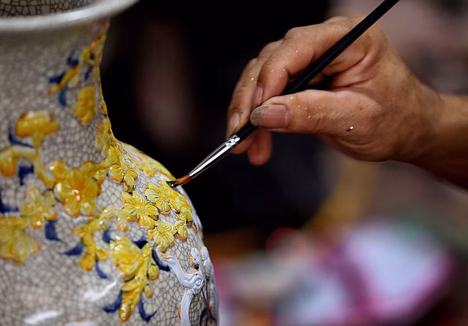 To create a smooth and shiny golden coat for products, gilding craftsmen need to overlay the products with super-thin gold leaves while the paintwork is still wet (Photo: Tran Viet/VNA)