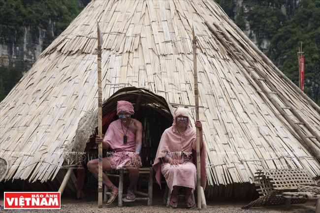 ​Luu Dinh Ton, 53, plays the village head (left) and one partner sitting in front of a hut for tourists to take photos (Source: VNA)