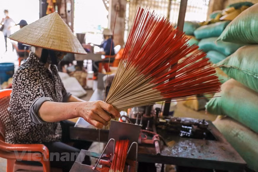 A woman rolls aromatic paste around bamboo sticks. Local people use ‘vau’ for making sticks since this variety of bamboo is highly flammable but not broken when burning. Before chopping, the bamboo trees are kept in certain substances for two months to protect them from weevils. With the help of machinery, the bamboo trees are chopped into uniform, round and glossy sticks. After that, the sticks are dipped in pink dye and dried outdoors. On average, Quang Phu Cau village buys around 200 tonnes of materials and produces 50 tonnes of incense a month. Undergoing many ups and downs, the incense production has helped improve local living standards significantly. (Photo: VietnamPlus)