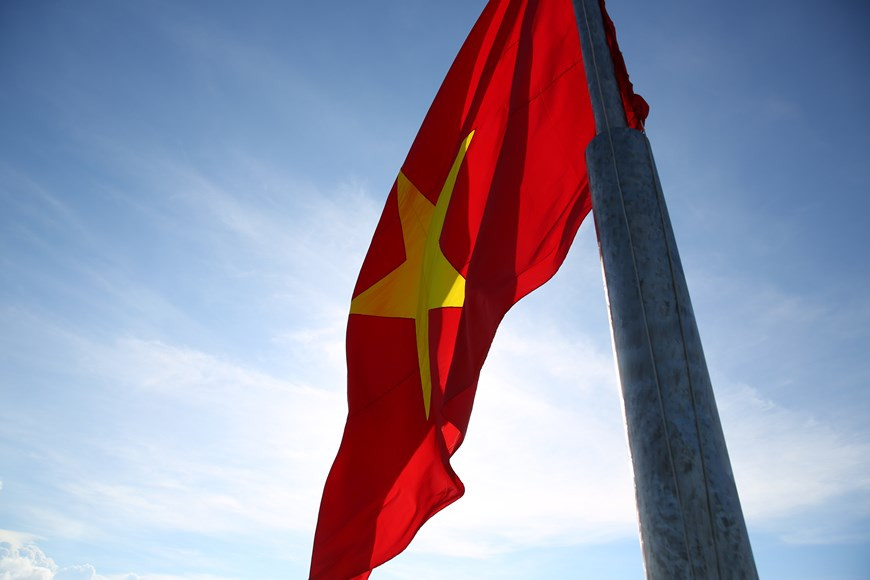 The sacred national flag flaps in the sky. The sacred national flag flies high in the sky. The national flag of Vietnam is rectangular in shape, its width is equal to two-thirds of its length, while in the middle of fresh red background is a bright five-pointed golden star. The red background is designed to symbolize the revolutionary zeal and all the blood and tear that was shed during the struggle for national liberation, while the yellow colour of the star symbolize the soul of the Vietnamese nation. The five-pointed golden star in the middle represents all the walks of life in the country uniting to defend and build the country. When the national flag of Vietnam flies, in the majestic National Anthem, everyone is filled with feelings of pride and gratitude as well as has a sense of their duty. (Photo: VietnamPlus)