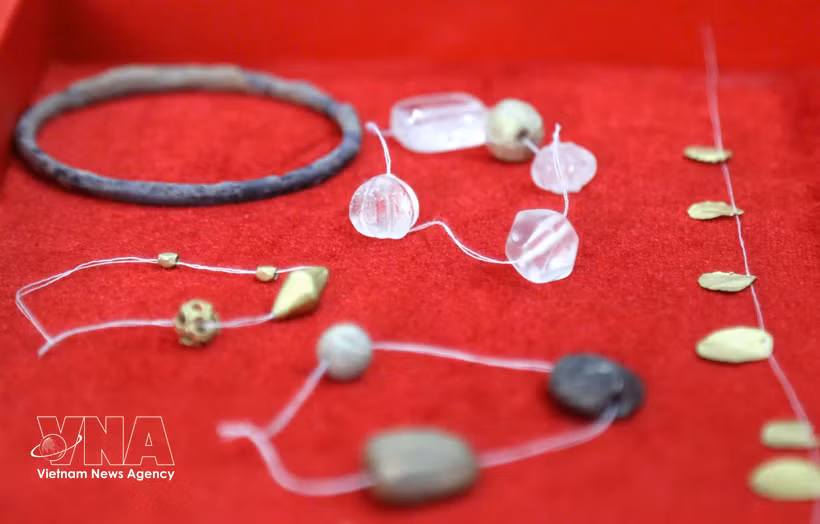 Glass beads, gold-coloured metal beads and leaf-shaped objects uncovered in the tombs. (Photo: VNA)