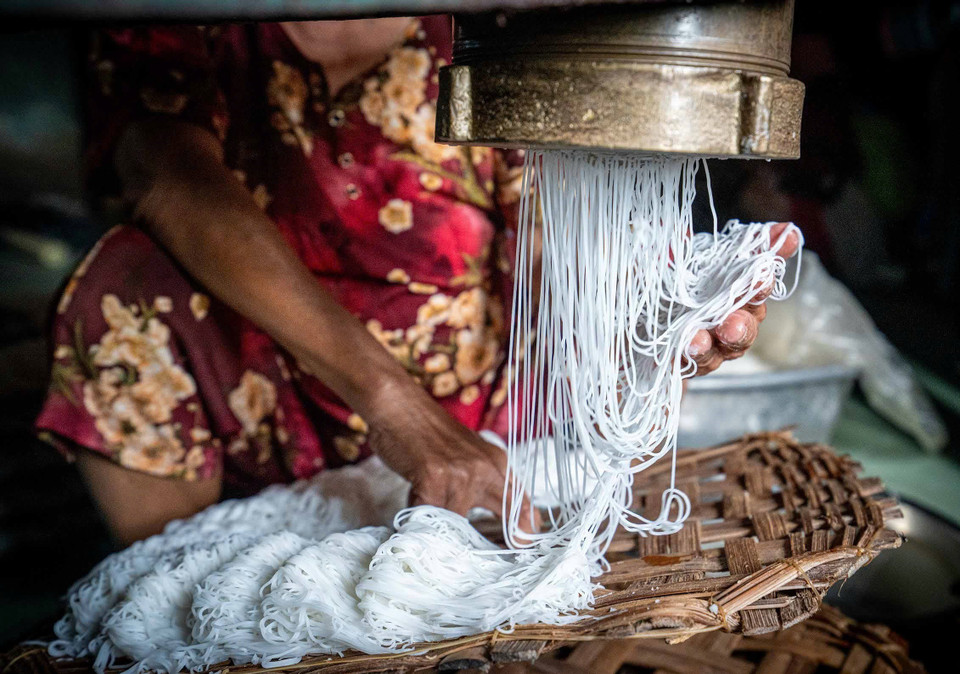 As the dough is pressed through the extruder, it emerges in fine strands. The artisan swiftly catches and separates them by hand into small, even portions, neatly arranged on bamboo trays. (Photo: Khanh Hoa - VNA)