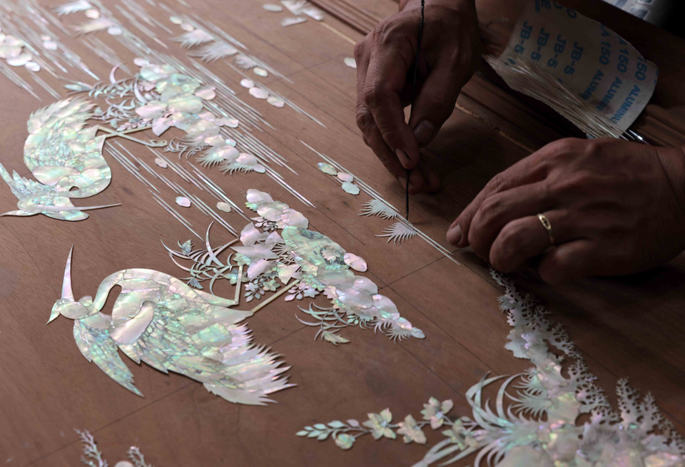 Placing mother-of-pearl pieces on wood before the carving process. (Photo: VNA)
