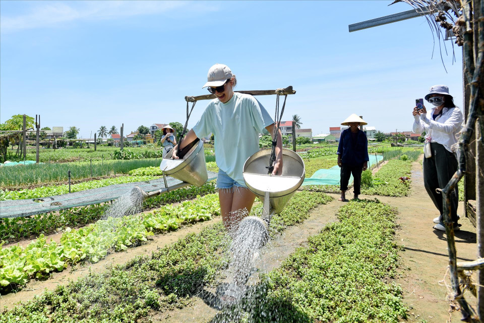Carrying two water buckets with a yoke on their shoulders proves to be a challenging yet interesting experience for foreign tourists. (Photo: Thanh Hoa/VNA)