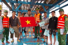 Officers of the Vam Lang border guard station in Dong Thap disseminate information on the prevention of illegal, unreported and unregulated (IUU) fishing and present a national flag to members of a local ship. (Photo: VNA)