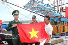 Fishermen receive national flag from a border officer (Photo: VNA)