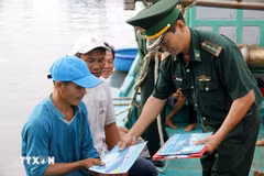A border guard distributes leaflets on anti-IUU fishing regulations to fishermen. (Photo: VNA)