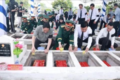 PM Pham Minh Chinh (first, left) and officials scatter flowers and earth to rebury martyrs' remains at the ceremony at the Doc Ba Dac cemetery in Thoi Son ward, An Giang province, on July 21. (Photo: VNA)