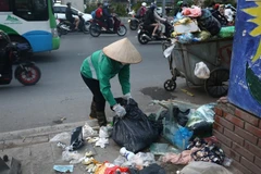 A sanitation worker collects rubbish at an informal dumping site in Hanoi (Photo: VNA)