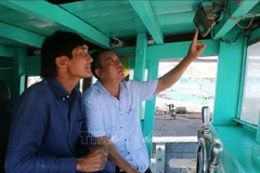 A representative of the Tran De fishing port management board inspects a vessel monitoring device on a fishing boat docked at the port. (Photo: VNA)