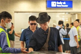 Passengers swipe their cards to board the train as instructed by staff (Photo: VNA)