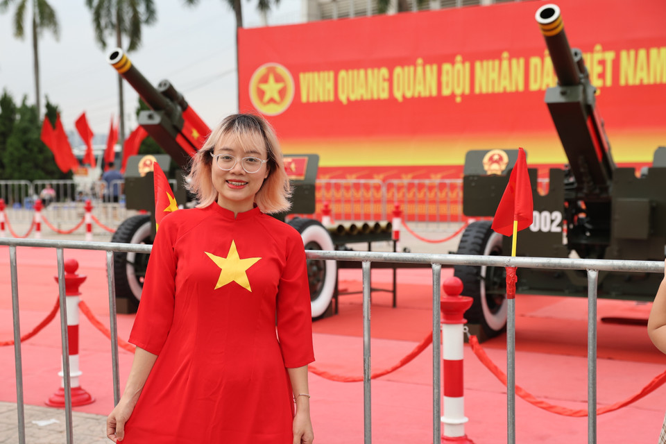 A young woman in a traditional ao dai patterned with the national flag smiles brightly beside the guns. (Photo: VNA)