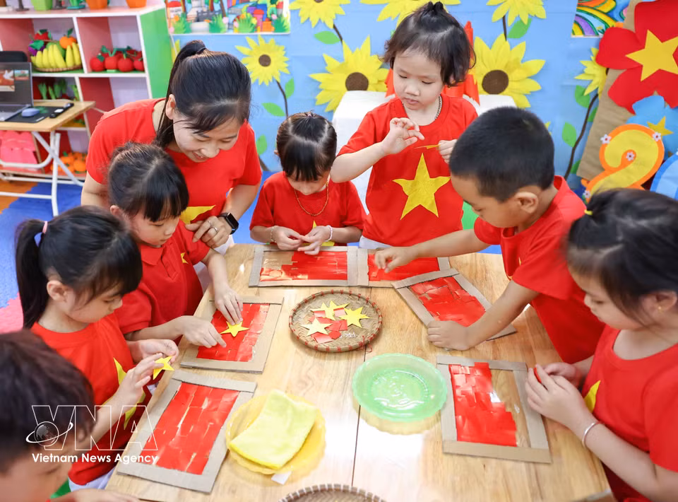 Preschool children carefully cut and paste materials to create bright and beloved national flags. (Photo: VNA)