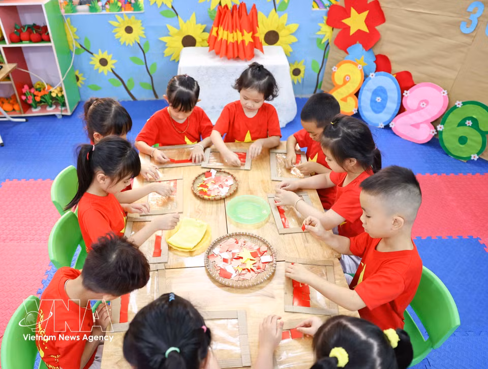 Preschool children carefully cut and paste materials to create bright and beloved national flags. (Photo: VNA)