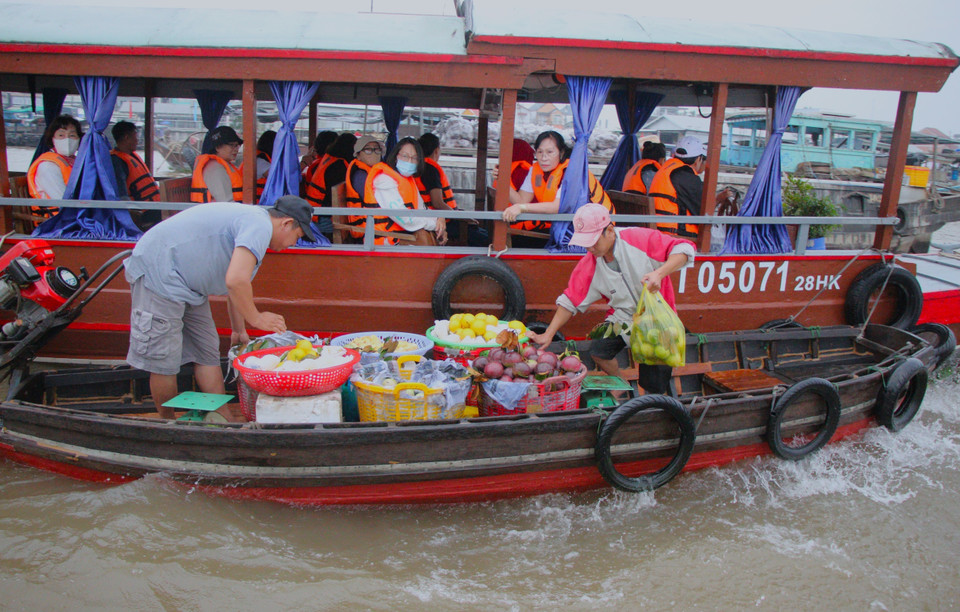 Visitors buy agricultural produce while touring Cai Rang floating market. (Photo: VNA)
