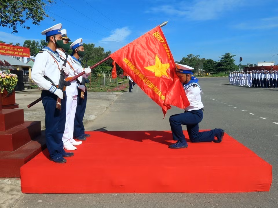 Newly-enlisted soldiers perform the tradition of kissing the National Flag during the oath-taking ceremony before departing for their assigned duties at units within Naval Zone 2. (Photo: VNA)